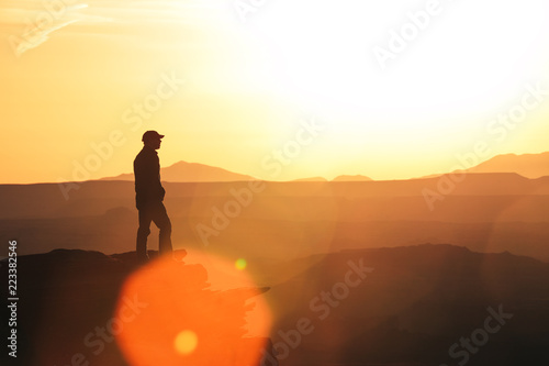 Man Silhouette On The Edge Of A Cliff Overlooking Utahs Canyonlands At Sunset With Layered Background photo