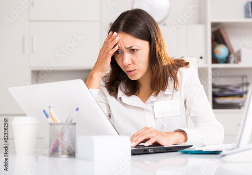 Tired young girl manager with laptop and documents  working at office
