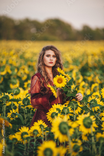 Young beautiful woman in a dress among blooming sunflowers. Agro-culture.