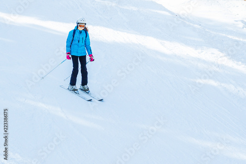a woman in blue in a ski suit and mask goes down on a snow skiing track. View from above.