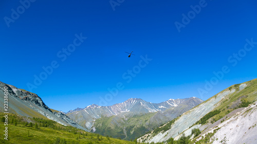 A helicopter in the sky above the mountains. A helicopter is flying over the tops of the mountains of Russia.
