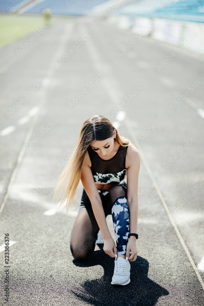 Fototapeta premium Female athlete tying her shoe laces on running track on a sunny day on stadium
