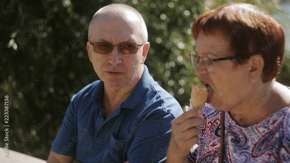 Elderly couple sitting on the promenade eating ice cream and talking. Elderly loving couple talking, and eating some ice cream cones. Elderly couple sitting on the promenade eating ice cream and talking. Elderly loving couple talking, and eating some ice cream cones.
