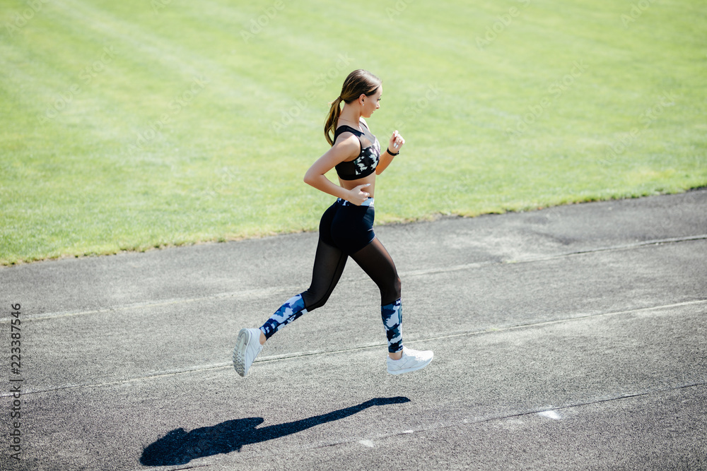 Young slim woman running on racetrack during training session. Female runner practicing on athletics race track.