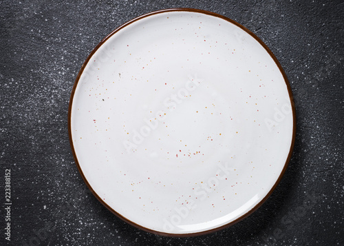 Empty white plate on dark stone table top view.
