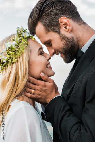 фотографія portrait of happy wedding couple in suit and white dress touching with noses on
