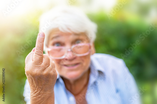 the old woman shows her middle finger. provocation disobedience attitude and offensive rude behavior concept. grandmother on nature