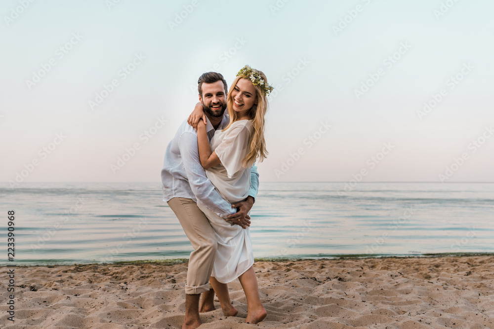 laughing bride and groom hugging and looking at camera on beach laughing bride and groom hugging and looking at camera on beach