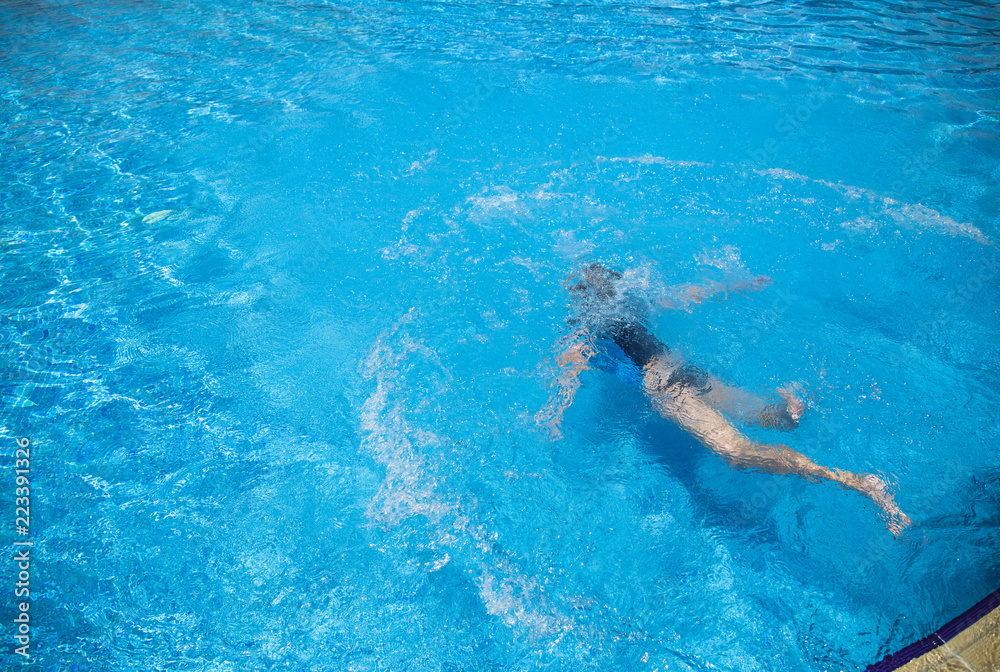 Top view of young kid swimming underwater in sunny summer pool outdoors at hotel resort. Horizontal color image.