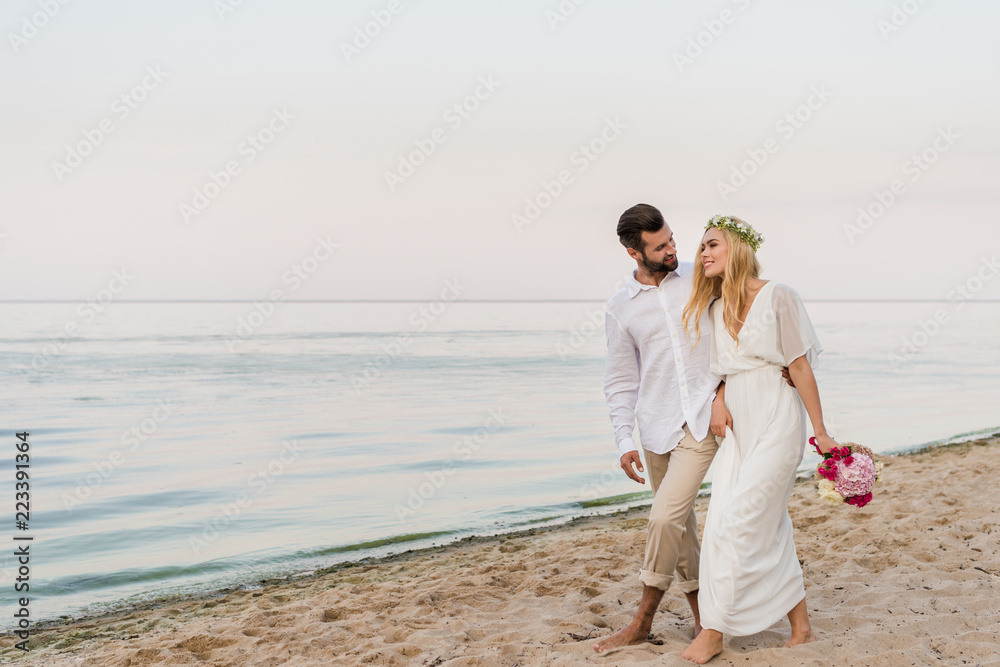smiling bride and groom hugging and walking on seashore smiling bride and groom hugging and walking on seashore