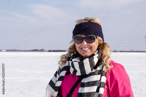 Attractive adult woman poses in farm field covered in snow on a cold winter day, wearing a ski jacket and hat © MelissaMN