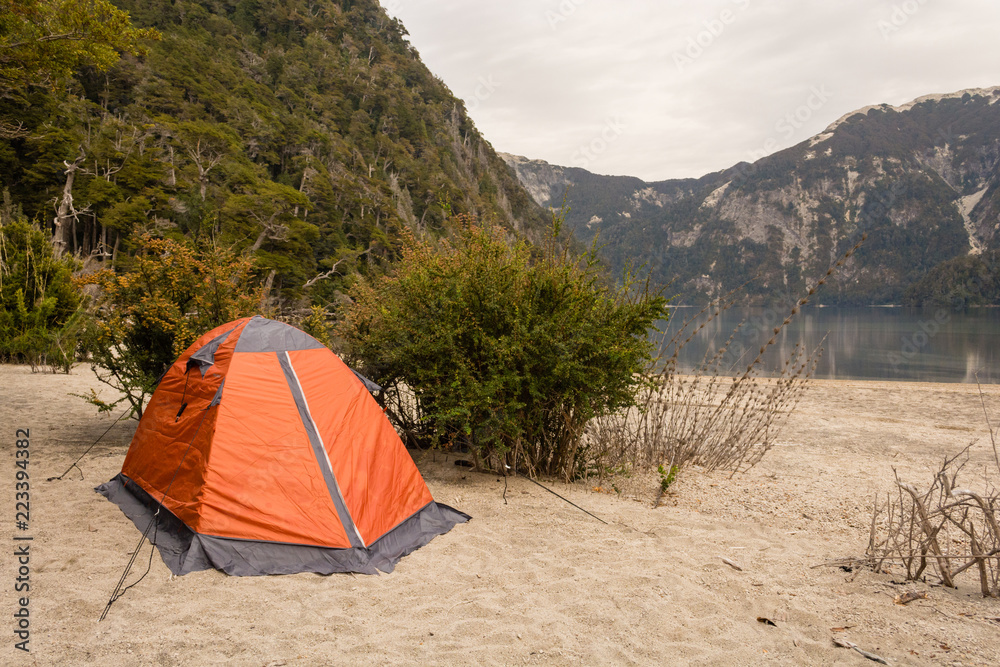 Camping orange tent in a campsite near a lagoon / Camping gear / Camping on the beach next to a lake with cloudy sky
