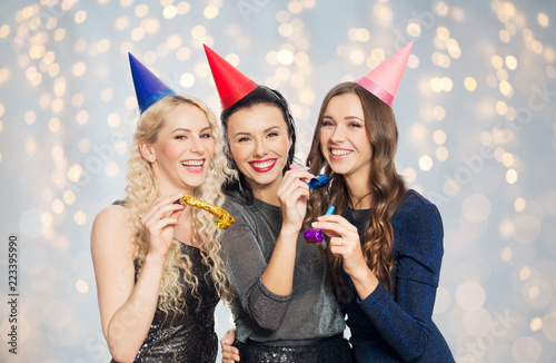people, celebration and holidays concept - happy women in party hats with blowers over lights background