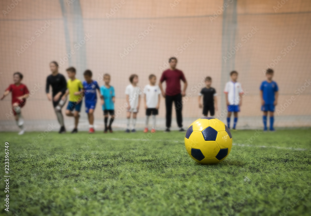 Traditional soccer ball on the football field on the background of children football players and their coach