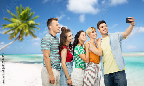 travel, technology and summer holidays concept - group of happy smiling friends taking selfie by smartphone over tropical beach background in french polynesia