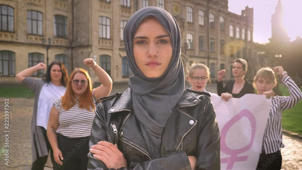 beautiful caucasian female in hijab standing with crossed hands in the middle of feminists demonstration on the street