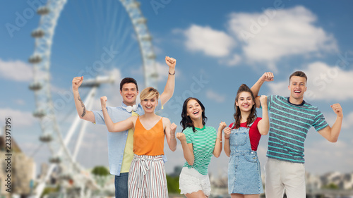 travel, tourism and entertainment concept - group of happy smiling friends making fist pump gesture over ferry wheel in london background