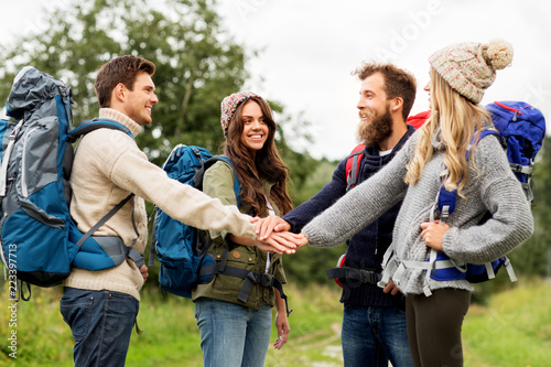 travel, tourism, hiking and people concept - group of smiling friends or travelers with backpacks stacking hands outdoors