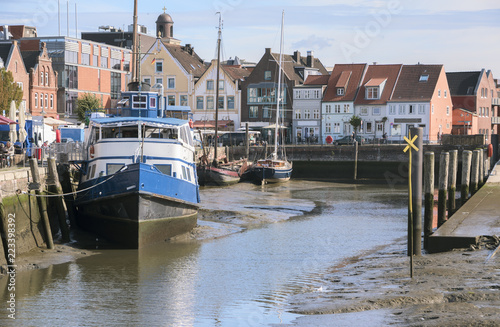 Inner harbor at low tide in the old town of Husum with boats on the mudflat and houses on a sunny day, north sea coast in germany