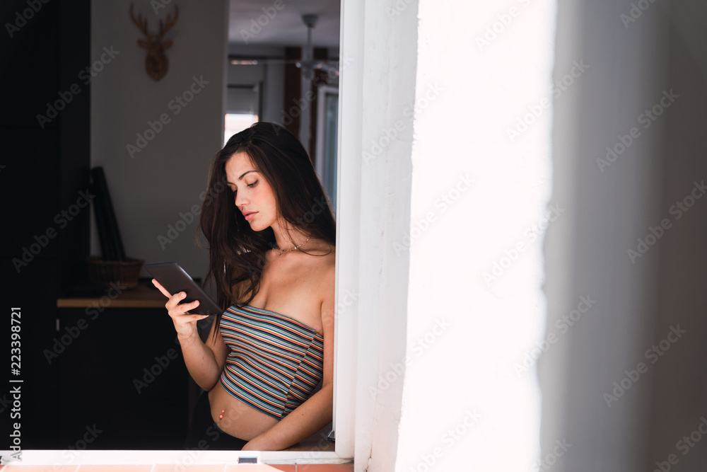 Young woman standing near window and using mobile phone Young woman standing near window and using mobile phone