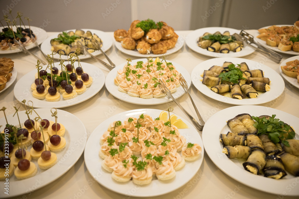 Row of plates with various cold appetizers standing on a table with a white tablecloth