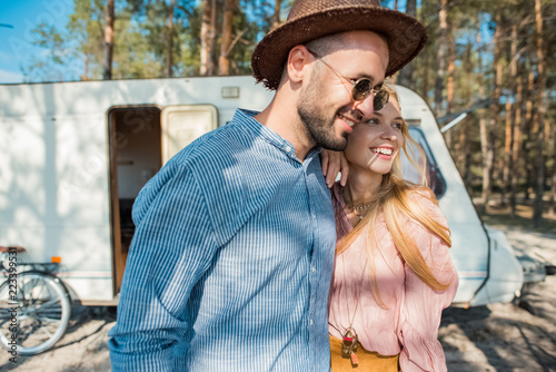 hippie couple embracing near trailer in forest