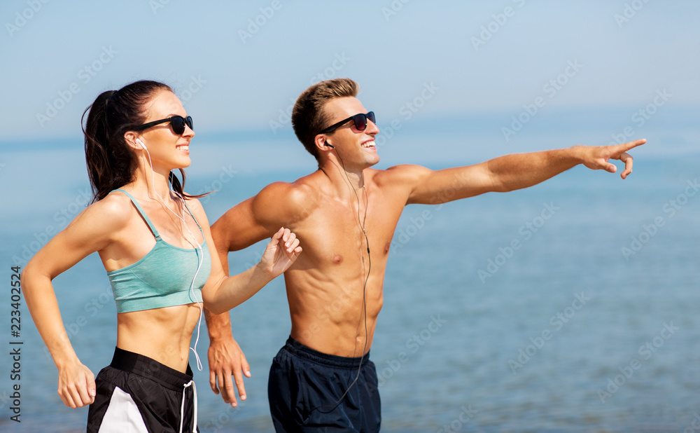 fitness, sport and technology concept - happy couple with earphones running along summer beach fitness, sport and technology concept - happy couple with earphones running along summer beach