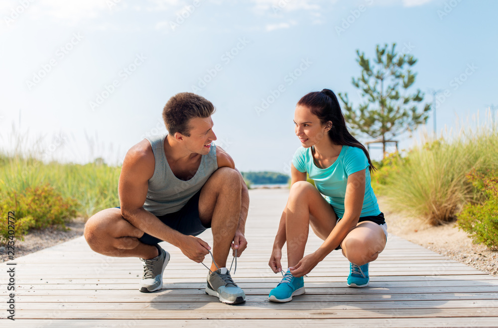 fitness, sport and lifestyle concept - couple of joggers tying sneakers shoelaces outdoors fitness, sport and lifestyle concept - couple of joggers tying sneakers shoelaces outdoors