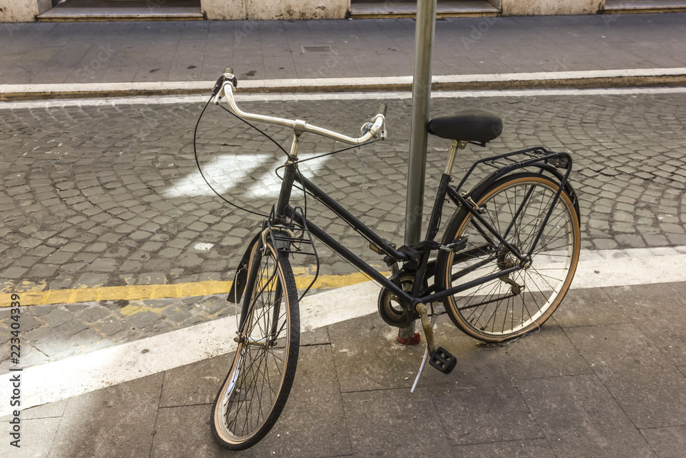 Broken retro bicycle with deflated and damaged wheel, enchained to the light pillar in the street of Rome