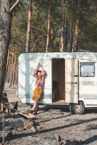 attractive hippie girl posing near campervan in forest