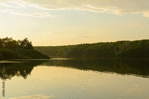 lake with a dense forest along the banks of a summer evening in golden color © alexnikit