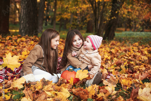 Three happy little sisters having fun playing with fallen golden leaves