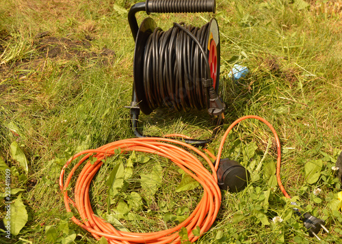 Coil with electric cable and extension cord on the grass, electric tools for construction works in the garden