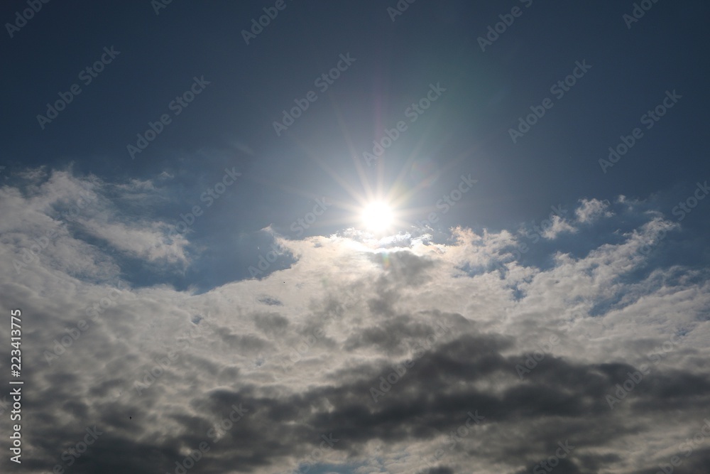 sun is shining behind white clouds at the blue sky sun is shining behind white clouds at the blue sky