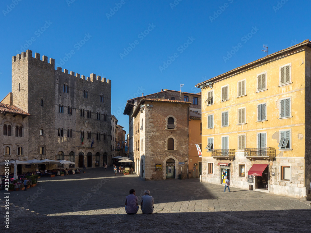 Leute schauen auf den hauptplatz mit umliegenden Gebäuden von Massa Marittima, Italien