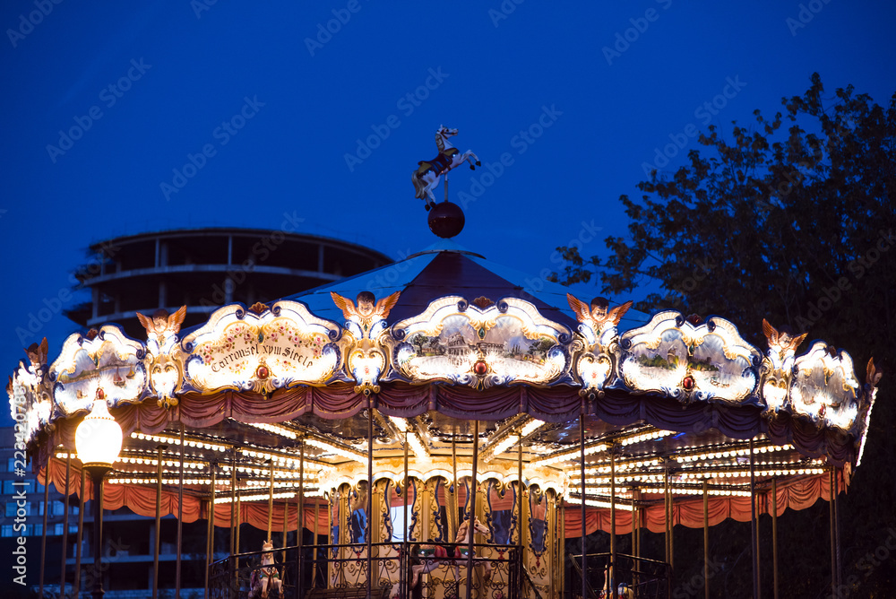 Children's Carousel at an amusement park in the evening and night illumination. amusement park at night. Outdoor vintage colorful carousel in the the city carousel detail. Vintage photo processing Children's Carousel at an amusement park in the evening and night illumination. amusement park at night. Outdoor vintage colorful carousel in the the city carousel detail. Vintage photo processing