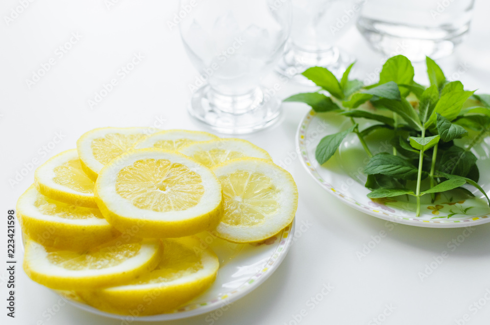 Summer set up from preparation refreshing drink with fresh mint leaves and juicy lemon slices with two glasses in the background. Summer set up from preparation refreshing drink with fresh mint leaves and juicy lemon slices with two glasses in the background.