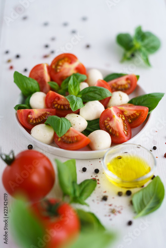 Caprese salad served on a white ceramic plate. White wooden background, high resolution