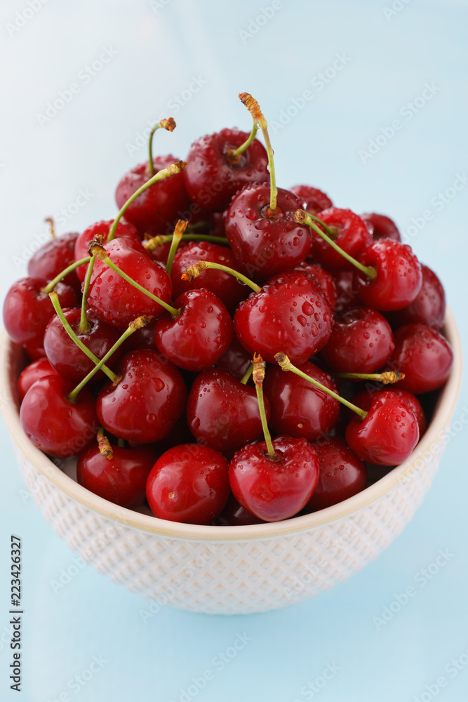 Ripe cherries in a white ceramic bowl. Blue background, high resolution Ripe cherries in a white ceramic bowl. Blue background, high resolution