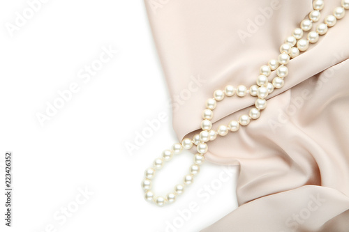 Pearl necklace with beige satin fabric on white background