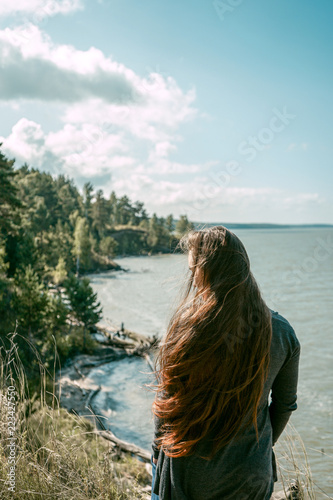 Summer lifestyle portrait in profile of beautiful young woman with perfect long hair fluttering in the wind. Standing on the coast on the river background. Romantic mood. Hair in the air © Kseniia