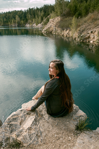Woman sits on rock in background of blue mountain lake. Stylish girl in nature, Siberia, Russia