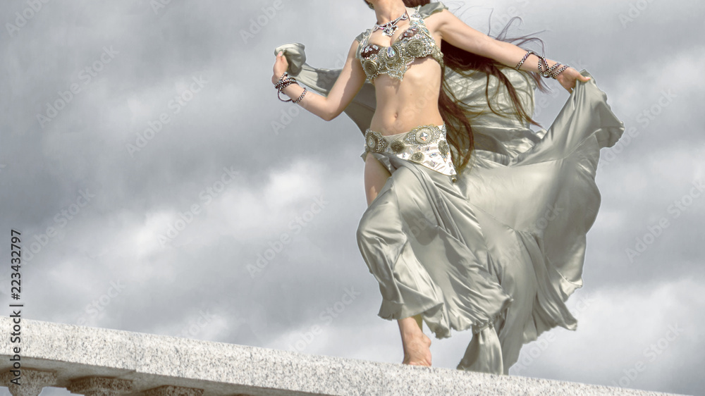 A girl in a silver costume for belly dancing stands in the wind in the rays of the autumn sun