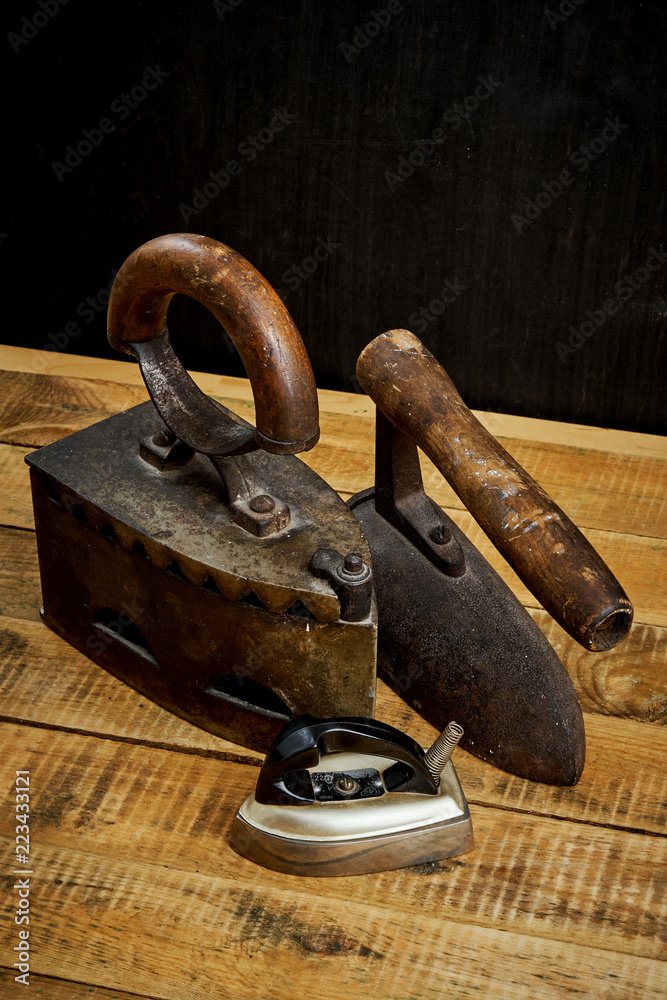 three old rusty iron on a bright wooden table next to a black wall three old rusty iron on a bright wooden table next to a black wall