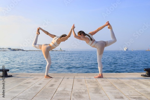 Fototapeta Naklejka Na Ścianę i Meble -  Two matching girls doing yoga dancer pose by water