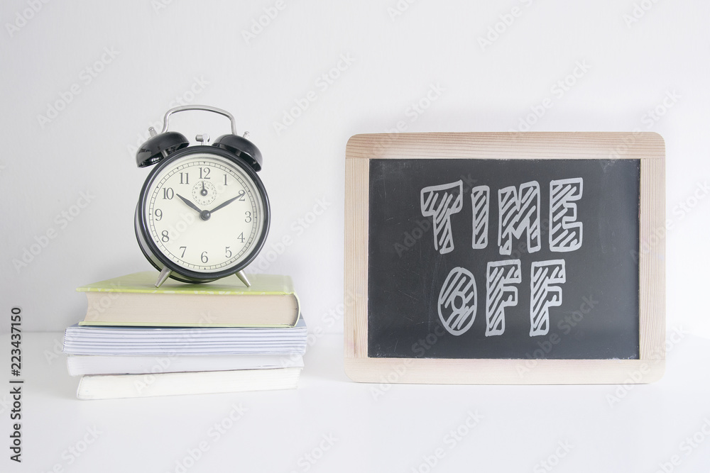 Alarm clock on a pile of books next to a blackboard with the text TIME OFF wrote on it. Empty copy space for Editor's text. Alarm clock on a pile of books next to a blackboard with the text TIME OFF wrote on it. Empty copy space for Editor's text.