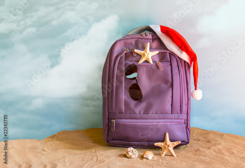 Santa Claus hat on backpack standing on sand beach. Christmas and New Year celebration. Nobody. photo