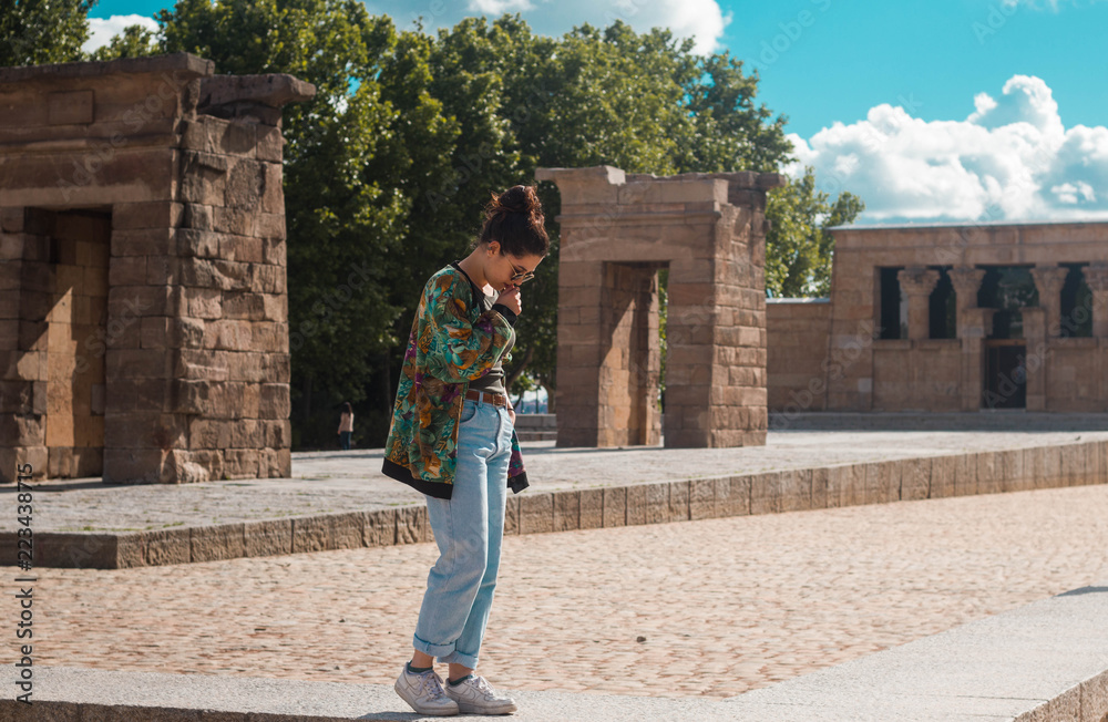 DEBOD TEMPLE, MADRID. SPAIN - JUNE 10, 2018. Young stylish woman with bun casual hairstyle admiring the iconic egyptian monument