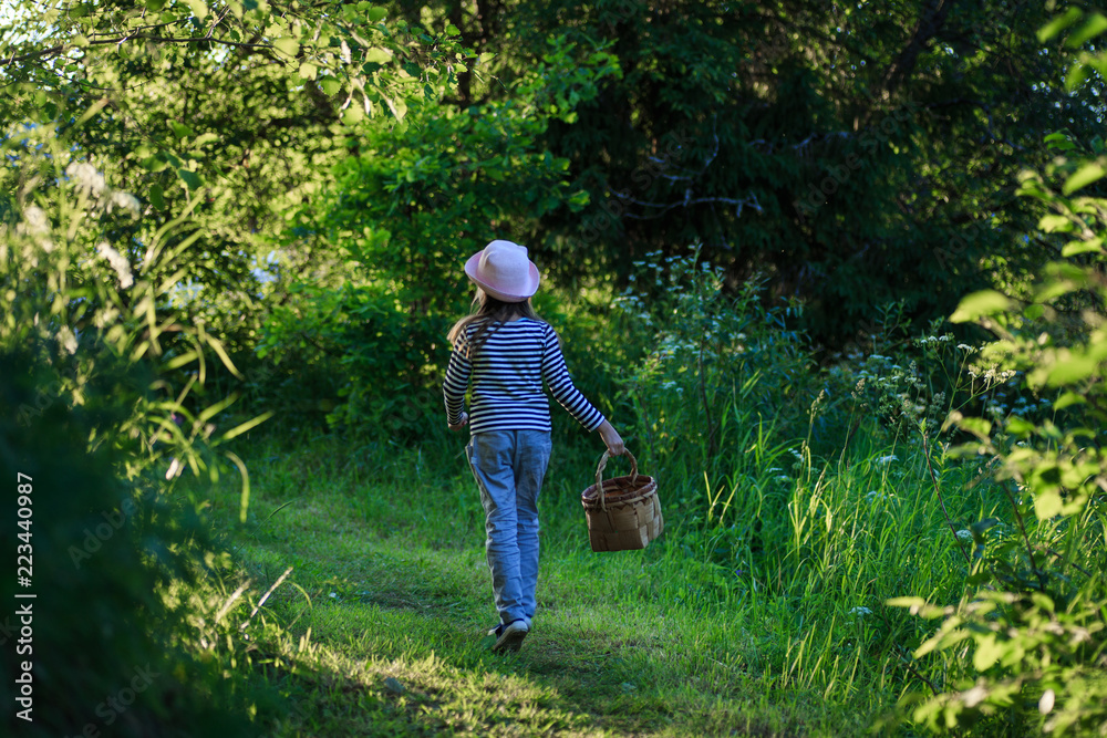 Young girl walking on a path through green woods carrying a birchbark basket