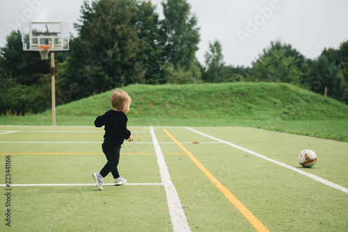 Cute one-year-old kid playing soccer with a ball on artificial grass